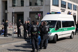 Eine Gruppe von Polizeibeamten steht vor einem Starbucks-Café mit einem Van auf der rechten Seite und einigen Menschen auf der linken Seite, mit einem Gebäude, einem Schild, einem Laternenpfahl und einem Zaun im Hintergrund.