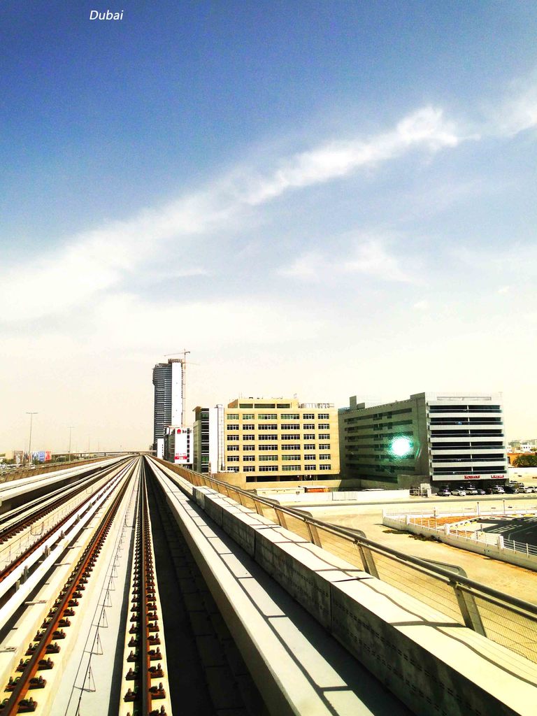 Eisenbahnschienen im Zentrum, mit Gebäuden und Straßen auf der rechten Seite und einem Himmel mit Wolken im Hintergrund.