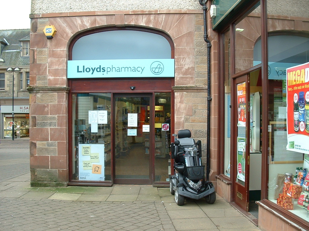 Eine Apotheke mit einem vor ihr geparkten Auto und einem Gebäude in der linken Ecke.