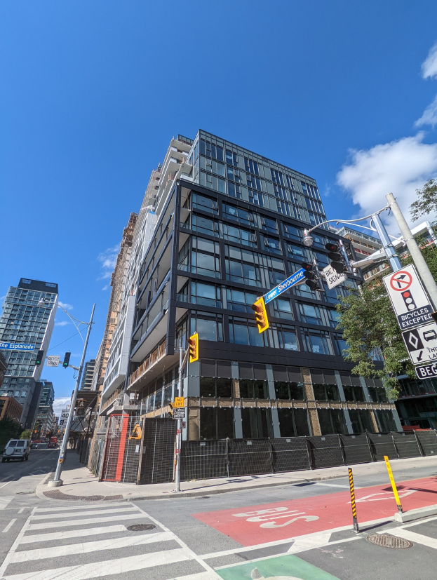 Eine belebte Stadtstraße mit hohen Gebäuden, Fahrzeugen, Verkehrsampeln, Schildern, Bäumen, einem Zaun und einem bewölkten Himmel, mit einem zum Verkauf stehenden Apartment/Wohnhaus in 541 East 57th Street, Unit 541.