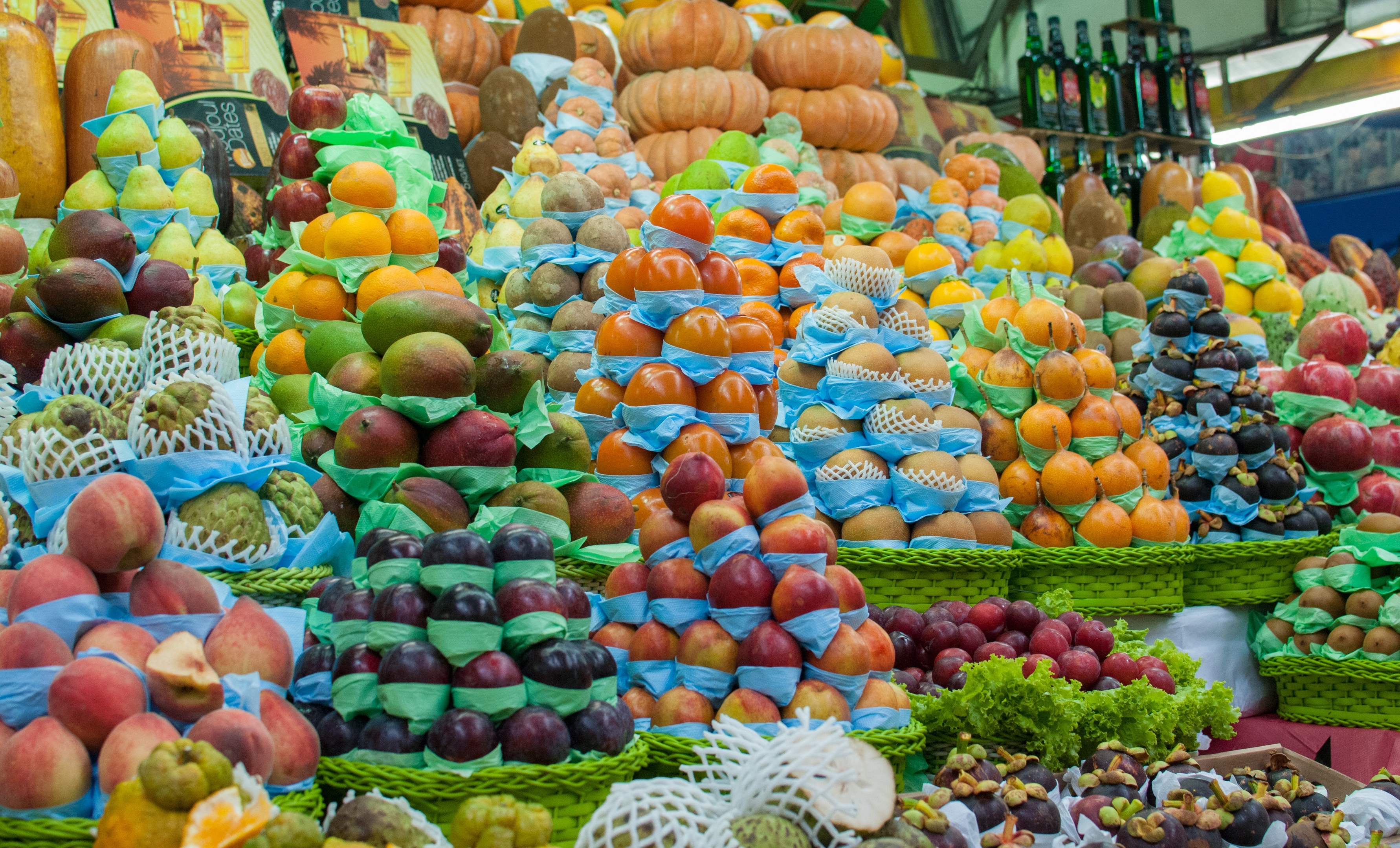 Ein Marktstand mit Äpfeln, Orangen, Birnen und anderem Obst sowie Flaschen auf Regalen unter heller Beleuchtung.