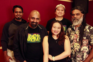 Eine Gruppe von Menschen, die zusammen in einem Aufnahmestudio stehen, lächeln und für ein Foto vor einer roten Wand posieren.