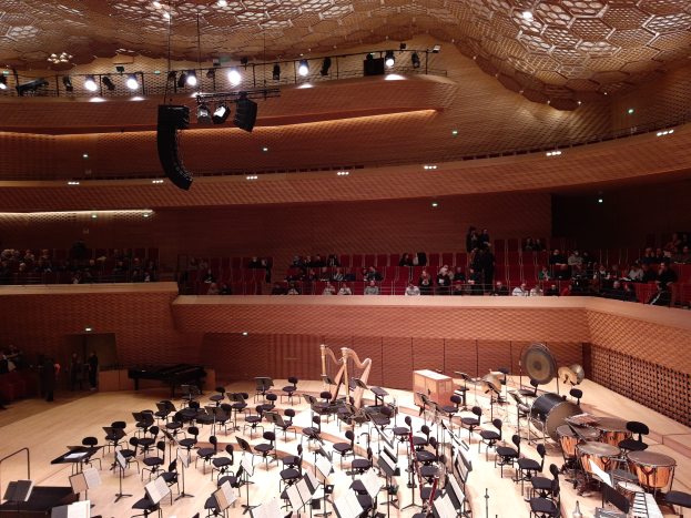 Ein großer Auditorium mit vielen Musikinstrumenten, Stühlen und Ständern mit Papieren und einer von Lampen beleuchteten Decke, darstellend den Großen Saal der Berliner Philharmonie.