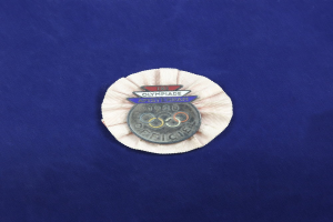 Blauer Stoff mit einem zentralen Olympischen Abzeichen, wahrscheinlich eine Medaille, das das Olympische Logo und Text zeigt.