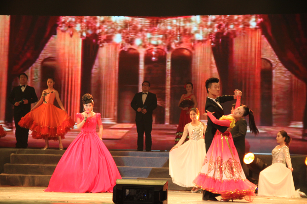 Eine Gruppe von Menschen auf einer Bühne mit Lichtern, Stufen und einem Hintergrundbild, mit einem Lautsprecher unten, was auf eine Tanzvorstellung hindeutet.