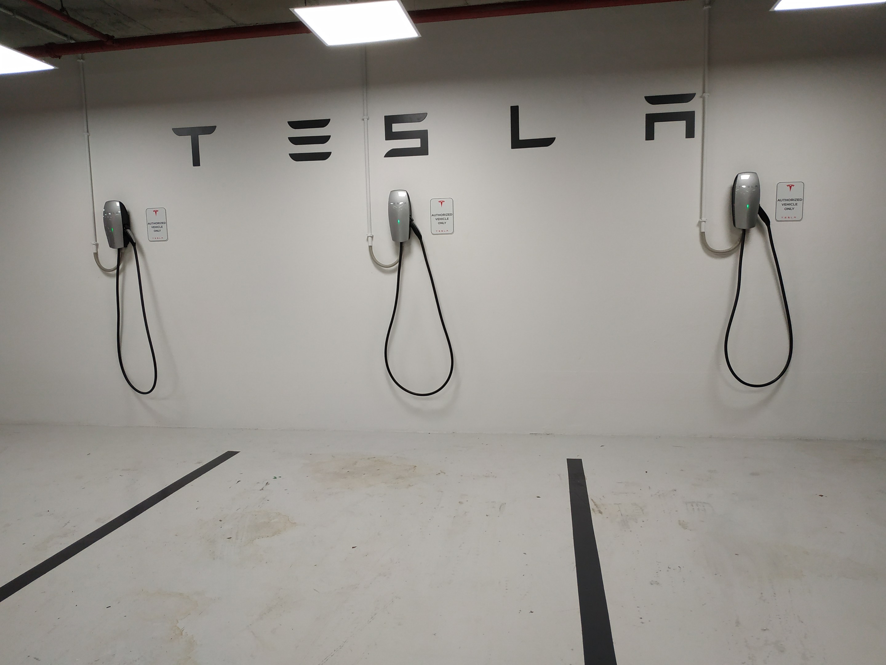 Eine Tesla-Ladestation in einer Tiefgarage mit angebrachten Kabeln und Deckenbeleuchtung, die die darunterliegende Etage zeigt.