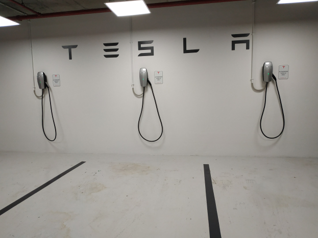Eine Tesla-Ladestation in einer Tiefgarage mit angebrachten Kabeln und Deckenbeleuchtung, die die darunterliegende Etage zeigt.