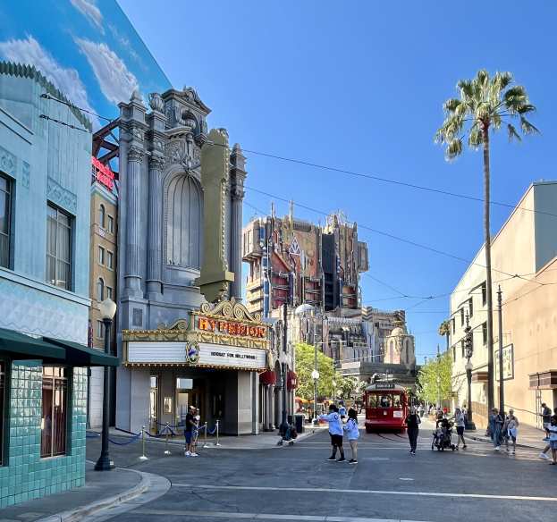Eine belebte Straßen Szene auf dem Universal Studios Hollywood mit Passanten, einem Fahrzeug und umliegenden städtischen Elementen unter einem sichtbaren Himmel.
