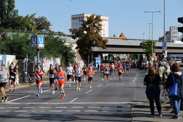 Gruppe von Menschen beim Marathonlauf auf einer baumgesäumten Straße unter einem klaren blauen Himmel.