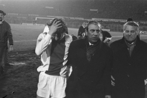 Schwarzes und weißes Foto einer Gruppe von Männern, die auf einem Fußballfeld stehen und bedrückt nach einem Matchsieg aussehen.