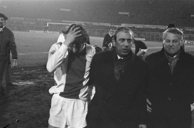 Schwarzes und weißes Foto einer Gruppe von Männern, die auf einem Fußballfeld stehen und bedrückt nach einem Matchsieg aussehen.