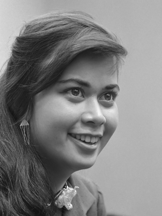 Eine Frau mit langen Haaren, die zu einem ordentlichen Knoten gebunden sind, lächelt warm in ein Schwarz-Weiß-Foto und schaut dem Betrachter direkt in die Augen.