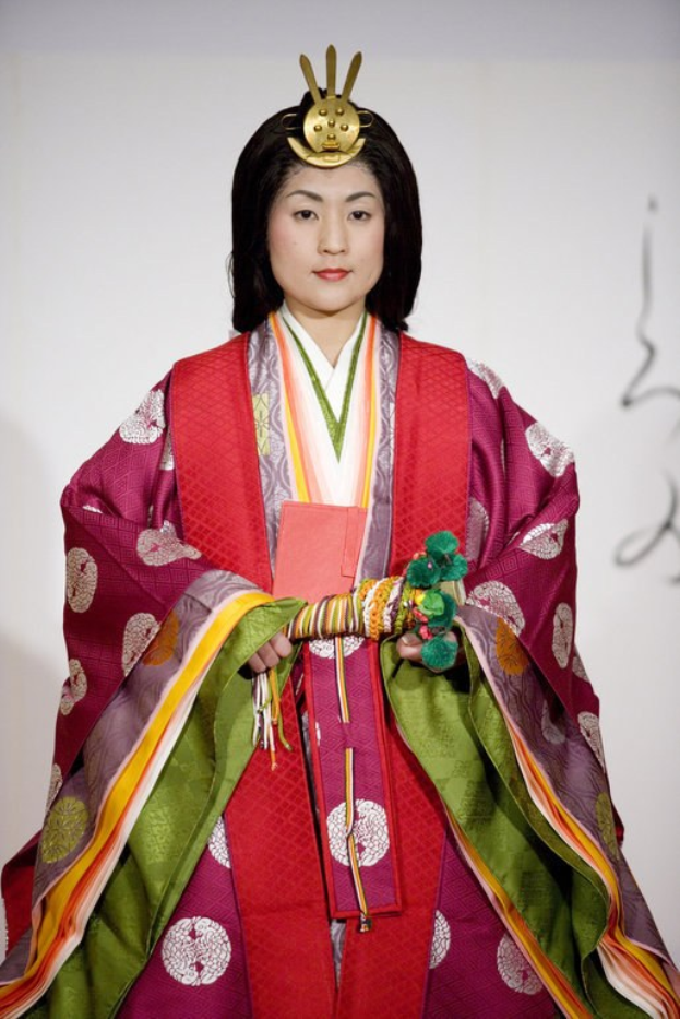 Eine Frau in einem traditionellen japanischen Kimono steht selbstbewusst auf einem Laufsteg, trägt ein leuchtend rotes und grünes Kleid mit aufwändigen Mustern und hat ihr Haar zu einem ordentlichen Knoten gebunden.