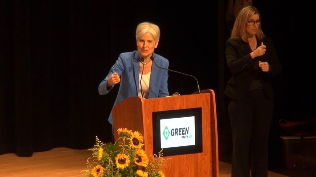 Zwei Frauen stehend an einem Rednerpult mit Mikrofon, Bildschirm und Blumen, wahrscheinlich auf einer Grünen-Parteiveranstaltung zum Thema Umwelt nachhaltigkeit.