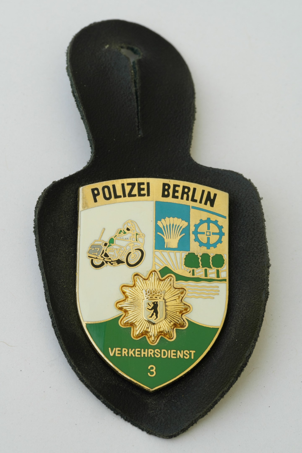 Ein schildförmiges Polizeibadgebnis mit der Aufschrift 'Polizei Berlin' auf blauem Hintergrund, weißem Rand, zentralem weißen Stern und schwarzer fetter Schrift, das auf einer Oberfläche liegt.