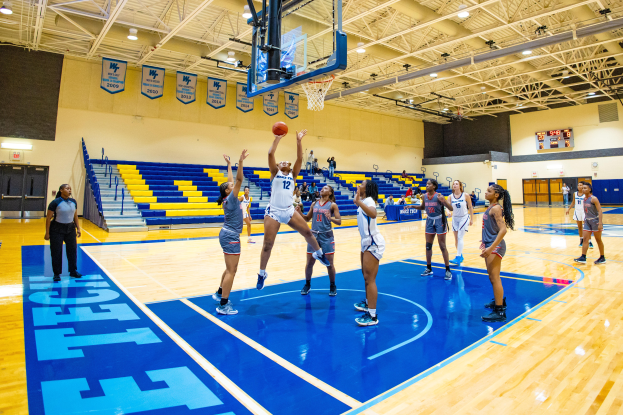 Eine Gruppe von Frauen, die Basketball in einer Turnhalle mit einem Scoreboard spielen.