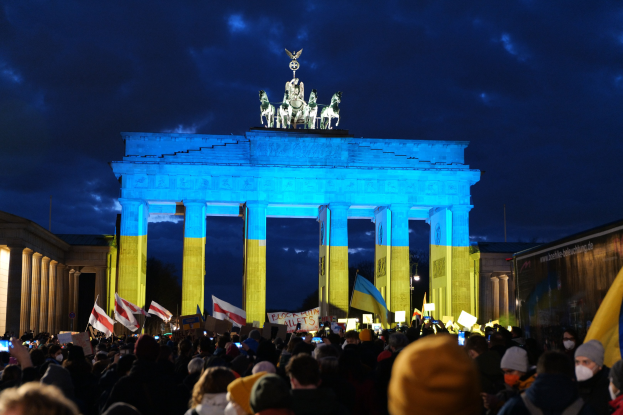 Menschenmenge mit Fahnen und Plakaten vor dem Brandenburger Tor mit einer Fahne auf der rechten Seite.
