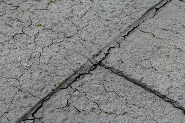 Nahaufnahme einer gebrochenen, verwitterten Straßenoberfläche mit tiefen, breiten Rissen und rauer, unebener Textur.