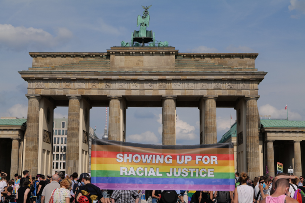 Eine Gruppe von Menschen steht vor dem Brandenburger Tor in Berlin, Deutschland, und hält eine Tafel mit der Aufschrift "Racial Justice."